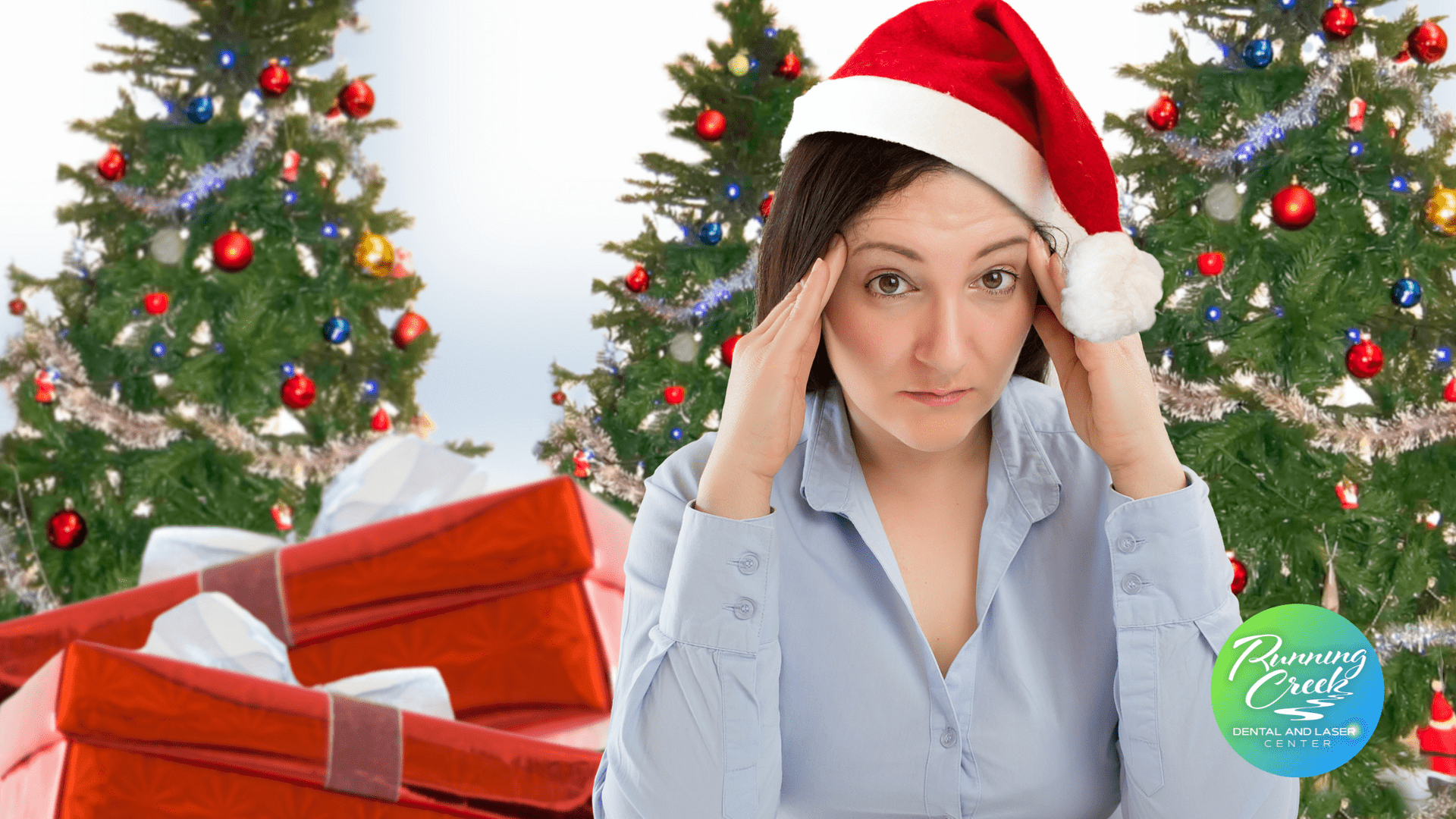 A woman wearing a santa hat is holding her head in front of a christmas tree.