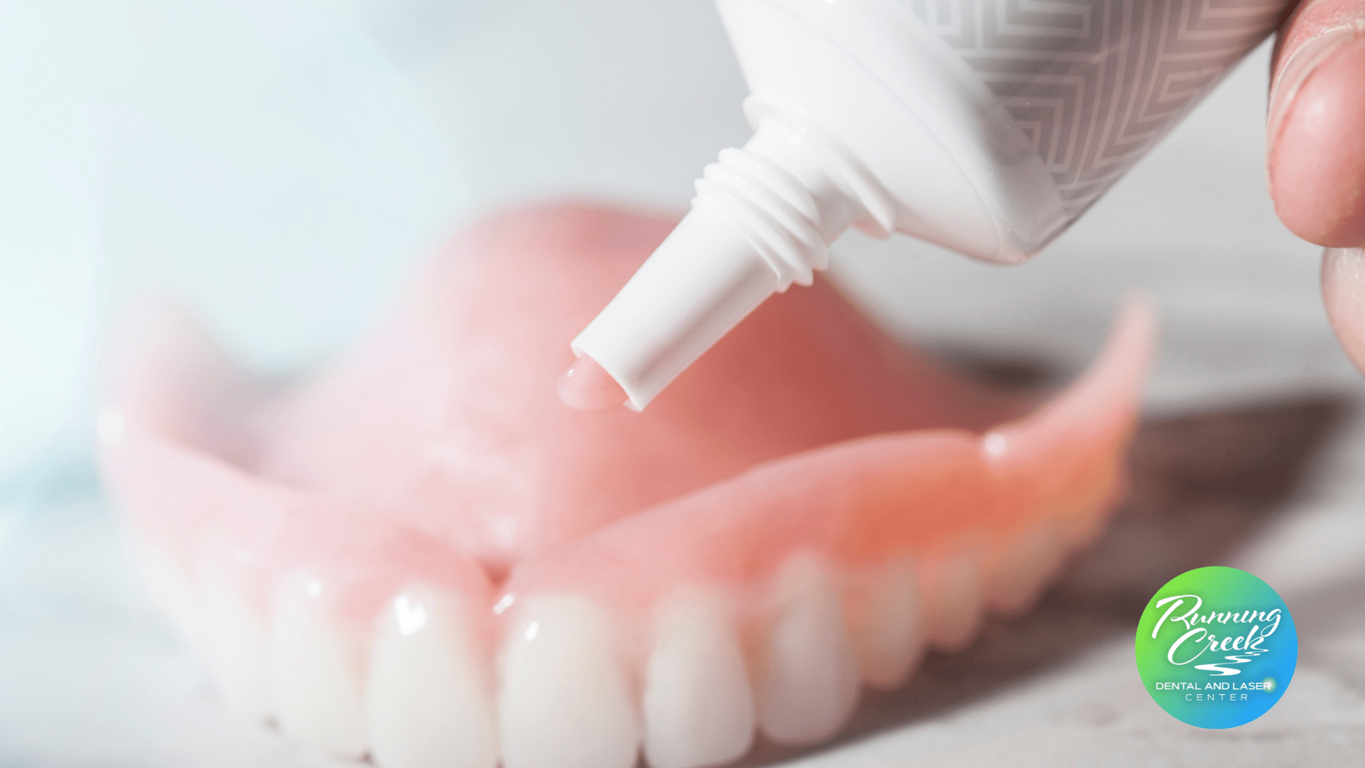 A person is applying toothpaste to a denture.