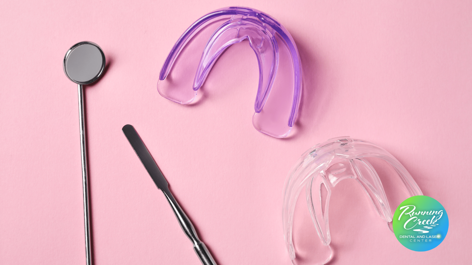 A pair of mouth guards , a dental mirror , and a spatula on a pink surface.