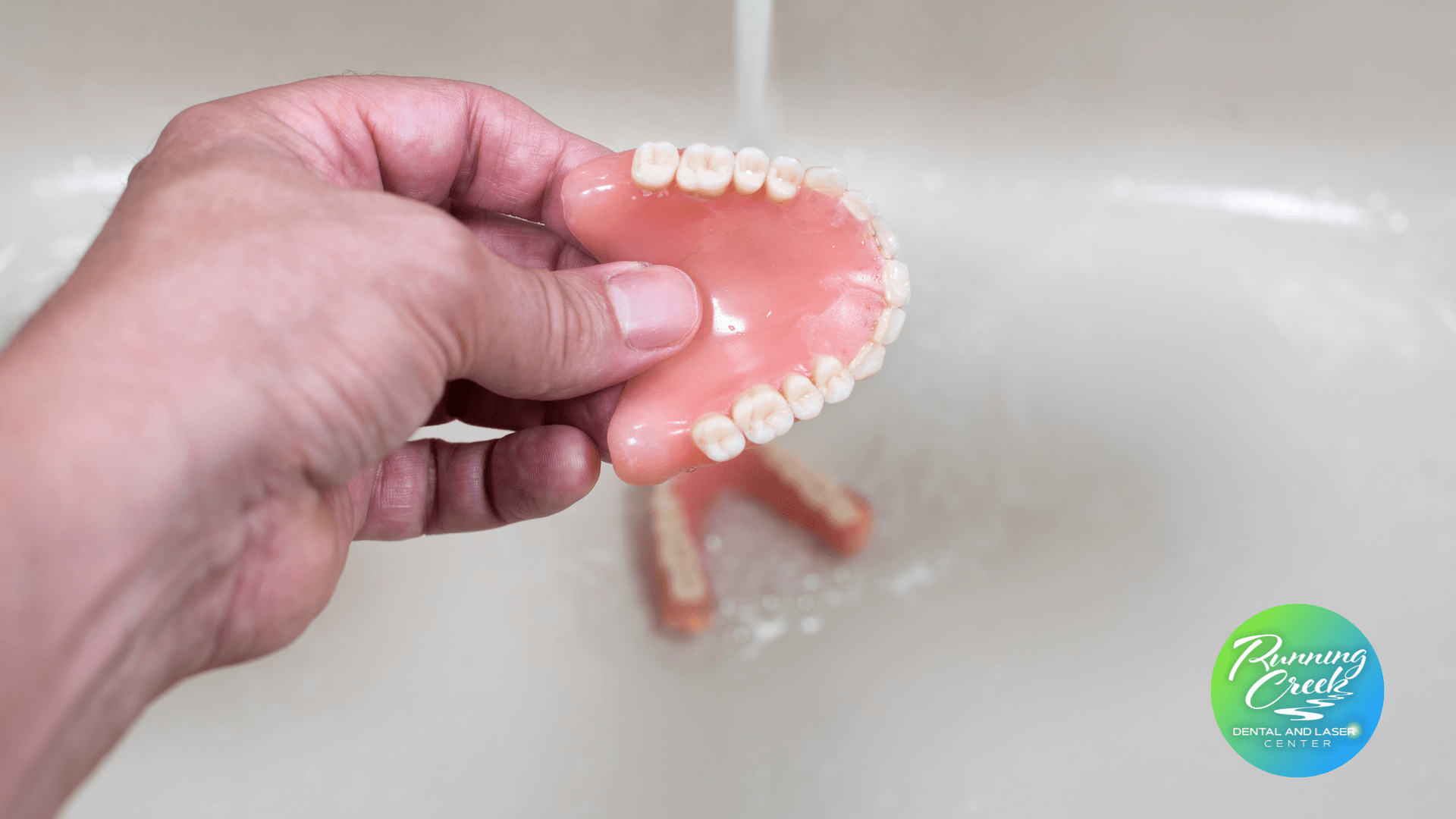 A person is washing a denture in a sink.