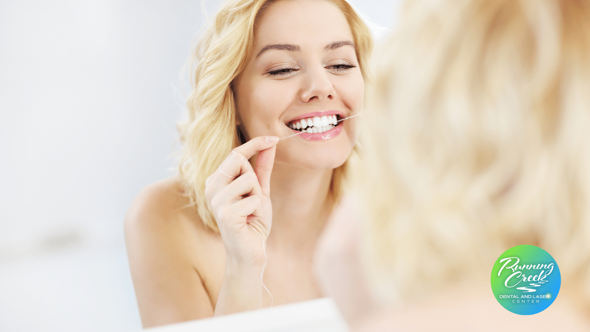 A woman is flossing her teeth in front of a mirror.