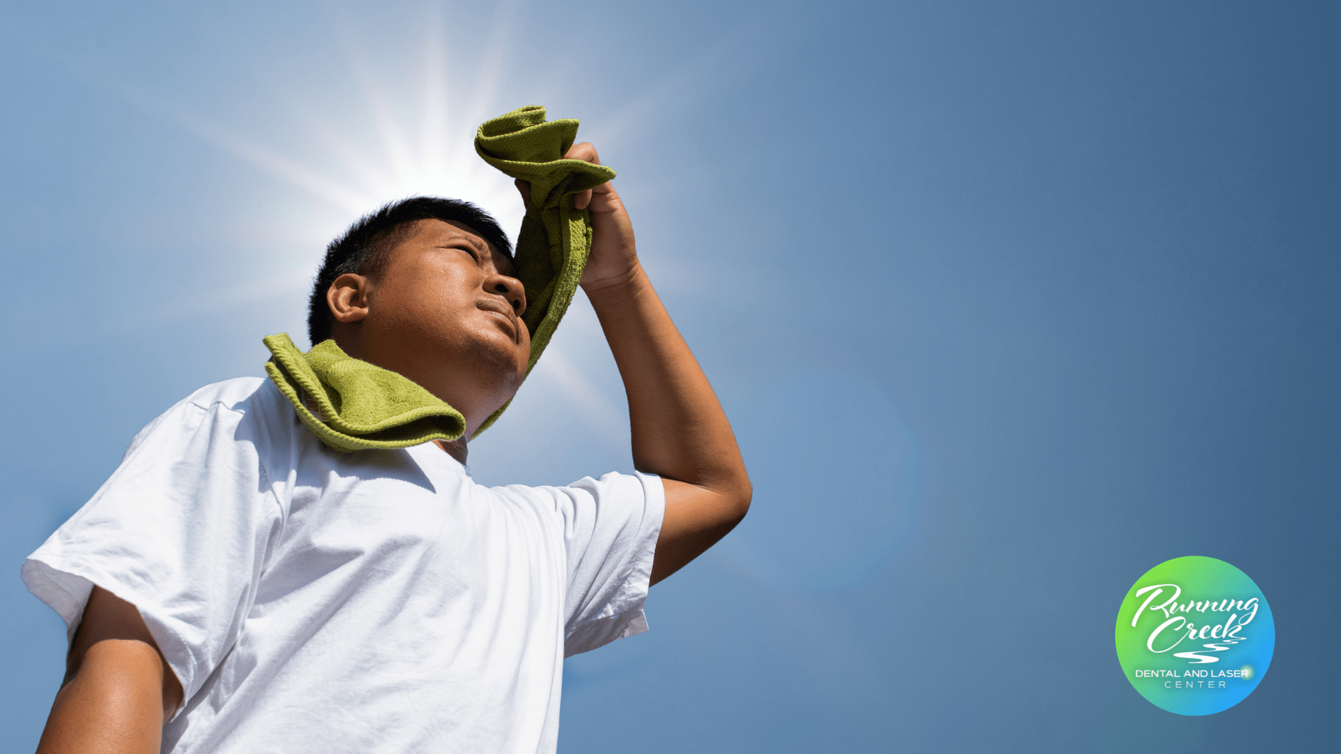 A man is wiping his face with a towel in the sun.
