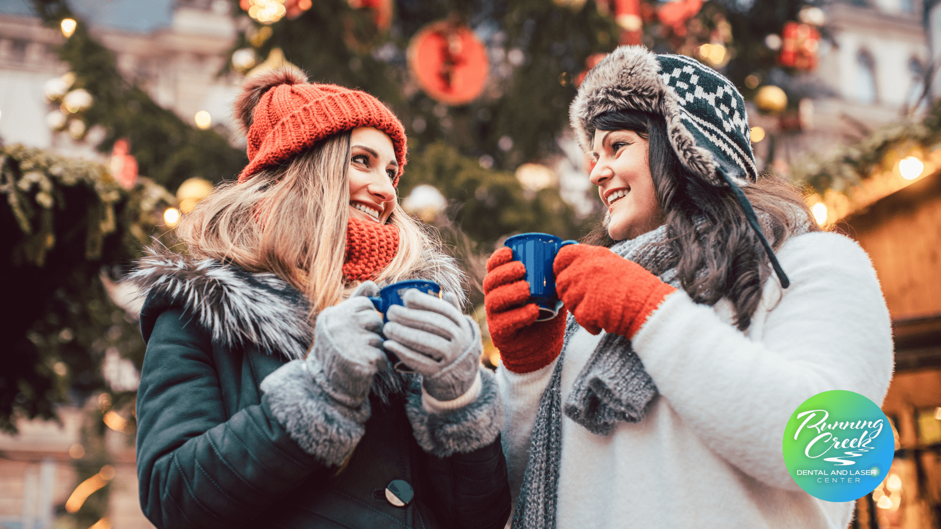 Two women are standing next to each other holding cups of coffee in front of a christmas tree.