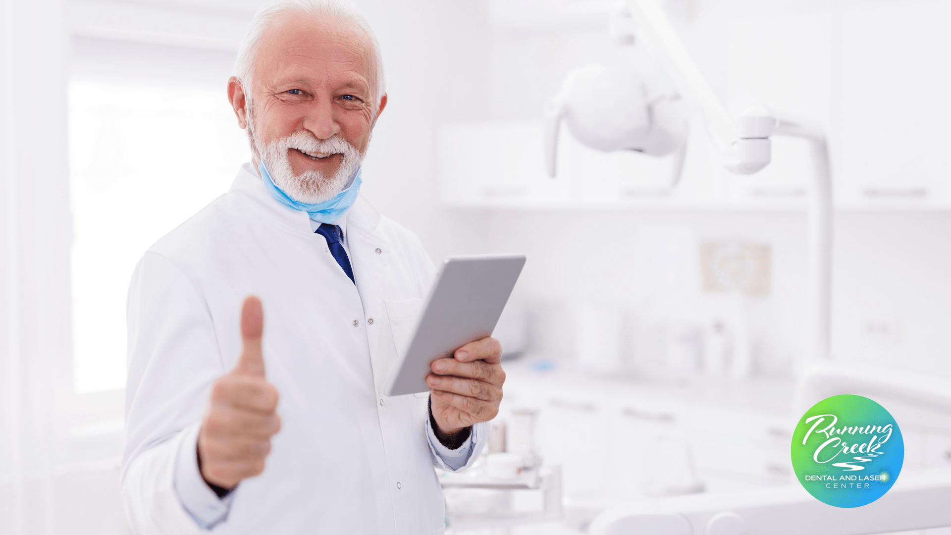 A dentist is holding a tablet and giving a thumbs up.